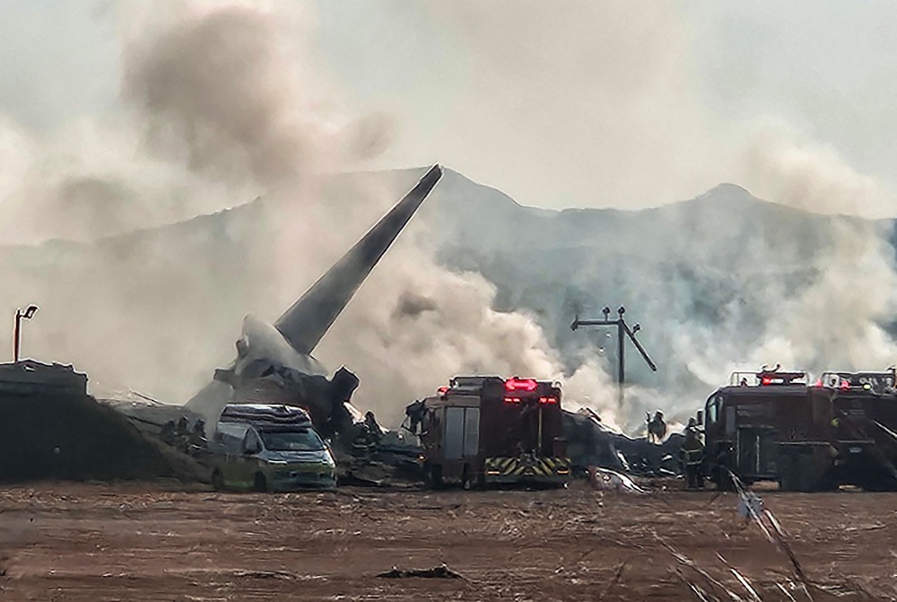 Smoke rises from the tail section of a Jeju Air Boeing 737-800 series aircraft after the plane crashed and burst into flames at Muan International Airport in South Jeolla Province, some 288 kilometres southwest of Seoul on December 29, 2024. (Photo by YONHAP / AFP) 