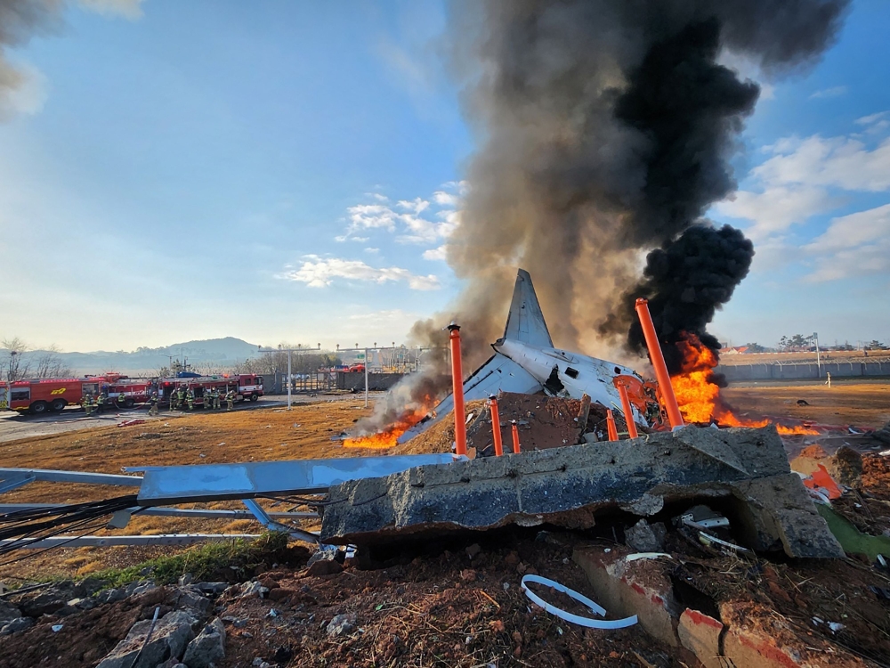 Fire and smoke rise from the tail section of a Jeju Air Boeing 737-800 series aircraft after the plane crashed and burst into flames at Muan International Airport in South Jeolla Province, some 288 kilometres southwest of Seoul on December 29, 2024. (Photo by YONHAP / AFP) 