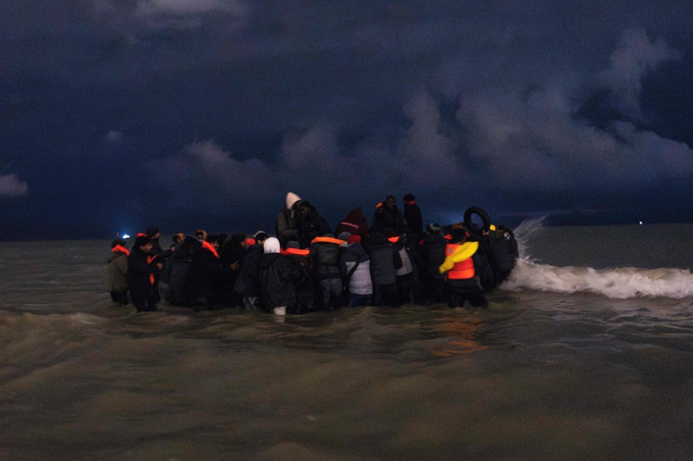 (Files) Migrants board a smuggler's inflatable dinghy in an attempt to cross the English Channel, on Bleriot beach at Sangatte, near Calais, northern France on October 30, 2024. (Photo by Sameer Al-Doumy / AFP)