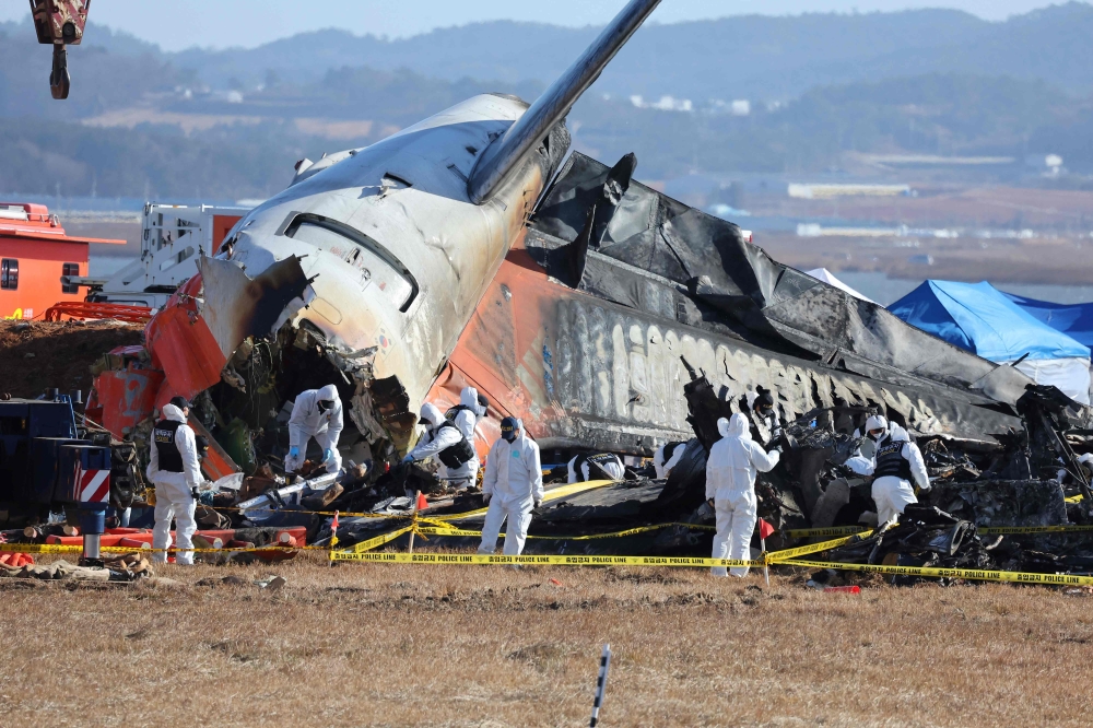 Police forensics personnel and National Bureau of Investigation officials work at the Jeju Air crash site in Muan on December 31, 2024. (Photo by YONHAP / AFP)