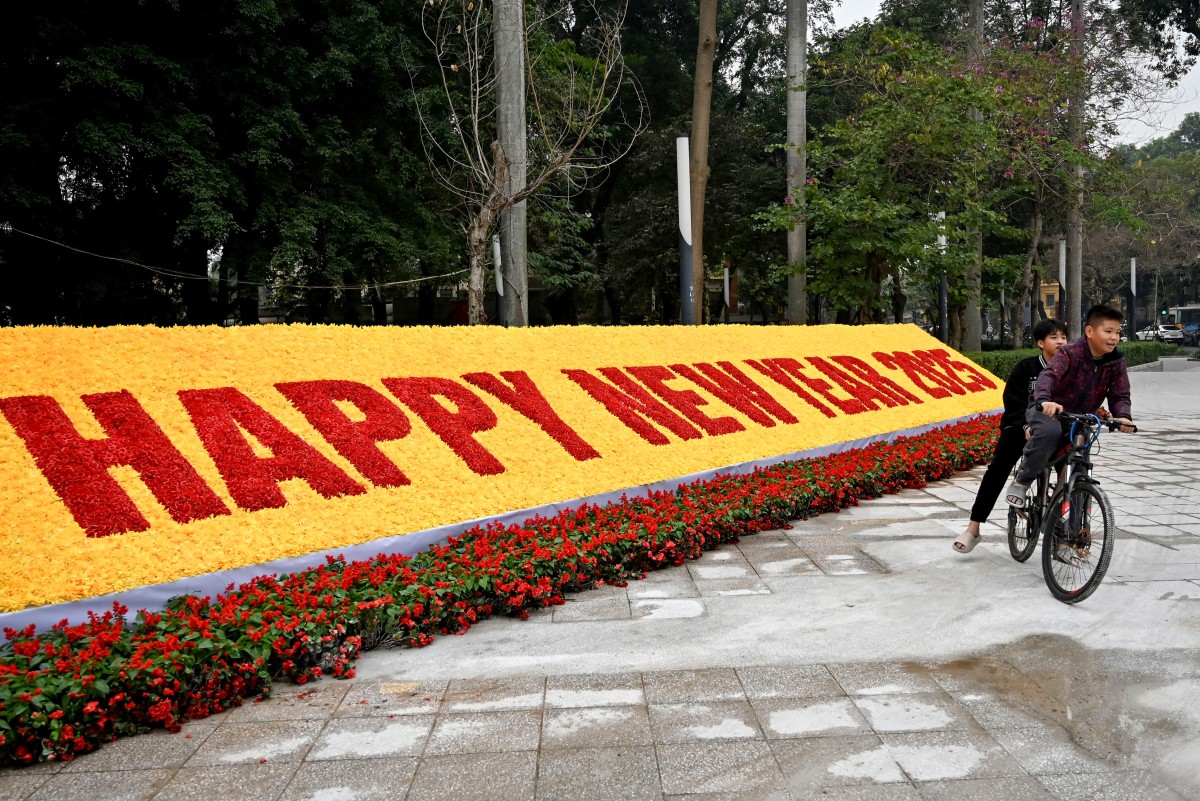 Photo used for representational purposes. Children ride their bicycle past a New Year 2025 numerals decoration made of plastic flowers in Hanoi on December 30, 2024. Photo by Nhac NGUYEN / AFP.
