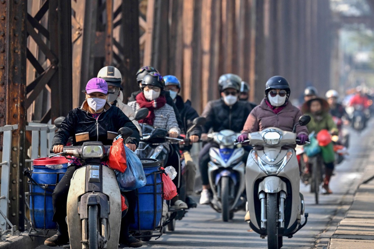 Motorists wearing face masks ride scooters along Long Bien Bridge amid heavy air pollution in Hanoi on January 3, 2025. Photo by Nhac NGUYEN / AFP