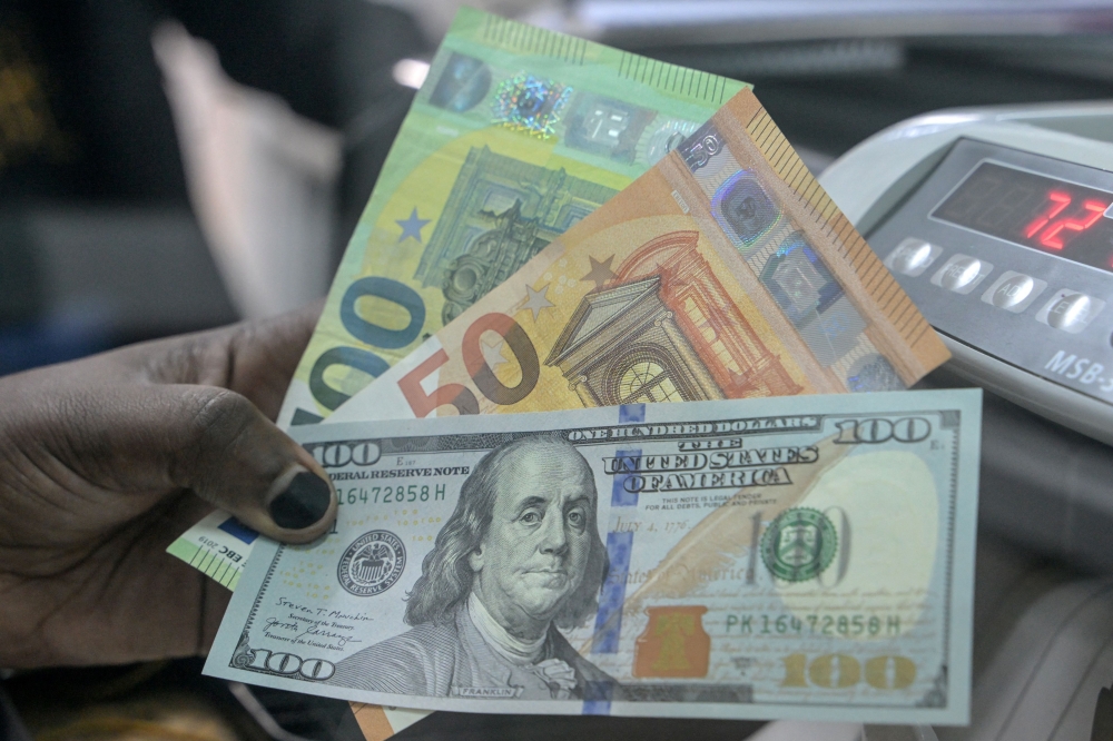 File: A teller displays US dollars and Euros at a money exchange market / AFP