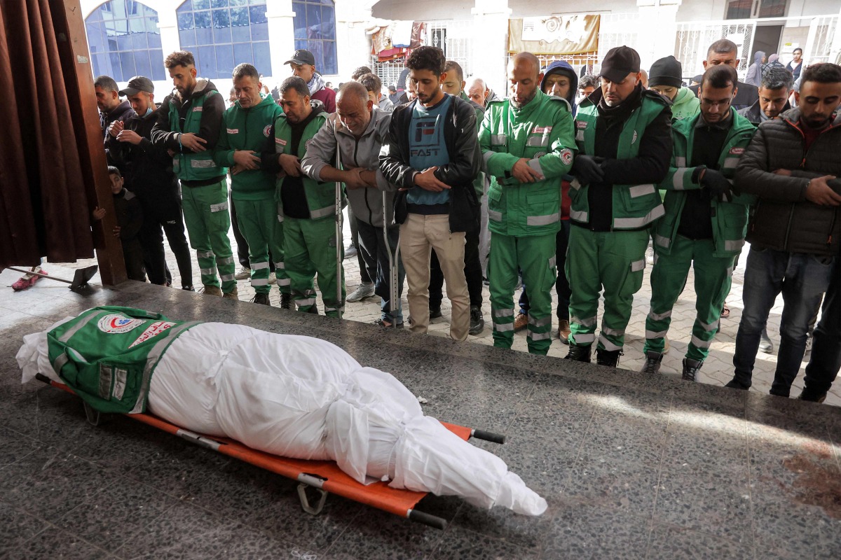 Palestinian Red Crescent paramedics pray by the body of their fallen colleague Mahmud al-Muhadad, who was reportedly killed in an Israeli air strike in Jabalia in the northern Gaza Strip, as it lies at the Ahli Arab hospital, also known as the Baptist hospital, in Gaza City on January 4, 2025. (Photo by Omar AL-QATTAA / AFP)
