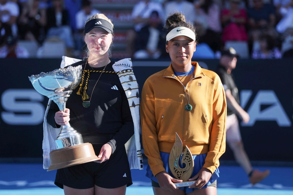 Clara Tauson of Denmark (L) celebrates with the trophy after her win over Naomi Osaka of Japan (R), following Osaka's retirement from their women's singles final match due to an abdominal injury, at the WTA Auckland Classic tennis tournament in Auckland on January 5, 2025. (Photo by Michael Bradley / AFP)