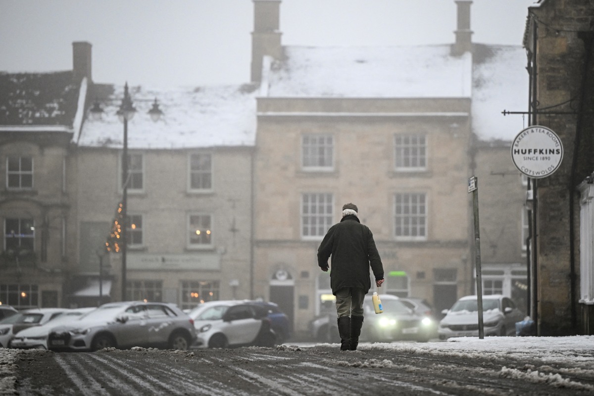 A pedestrian carries a milk bottle across the covered in snow streets of Stow-on-the-Wold, central England, on January 5, 2025 as heavy snow across parts of England are set to cause disruption. Photo by JUSTIN TALLIS / AFP