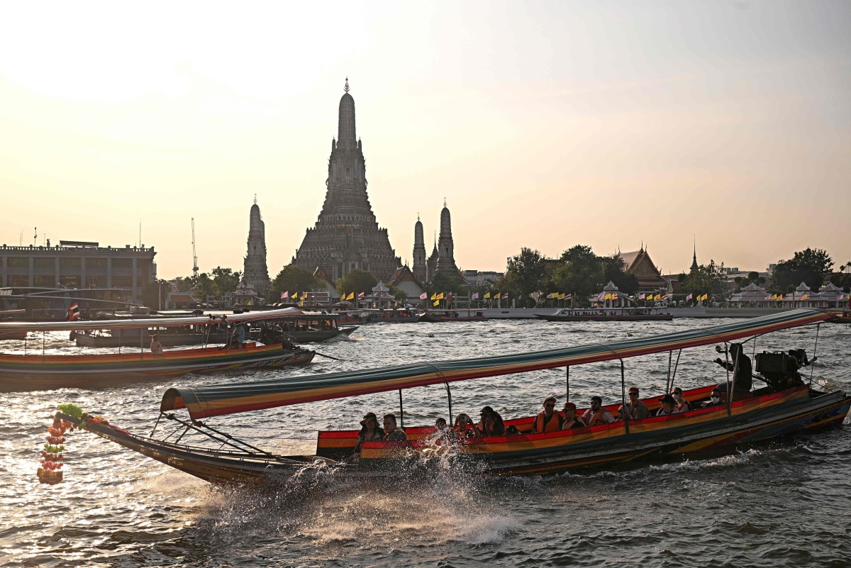 Tourists ride a longtail boat past Wat Arun temple along the Chao Praya river in Bangkok on December 19, 2024. Photo by Lillian SUWANRUMPHA / AFP