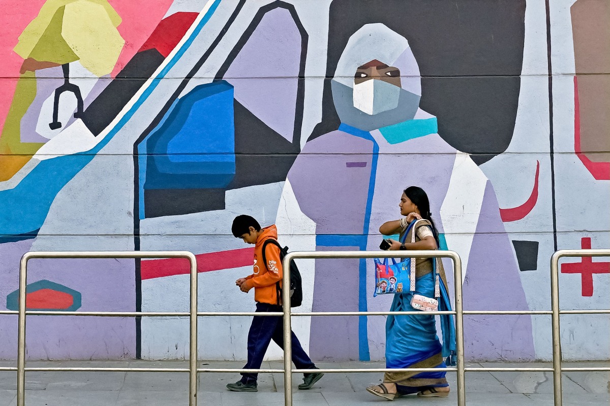 Pedestrians walk past a wall mural promoting awareness on using face masks, in Bengaluru on January 6, 2025. Photo by Idrees MOHAMMED / AFP