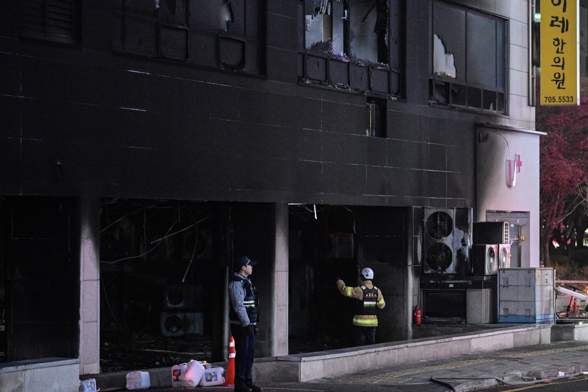 Firefighters and a police officer stand in front of a commercial building that was damaged by a fire that broke out at the Bundang district in Seongnam on January 3, 2025. (Photo by Philip FONG / AFP)
