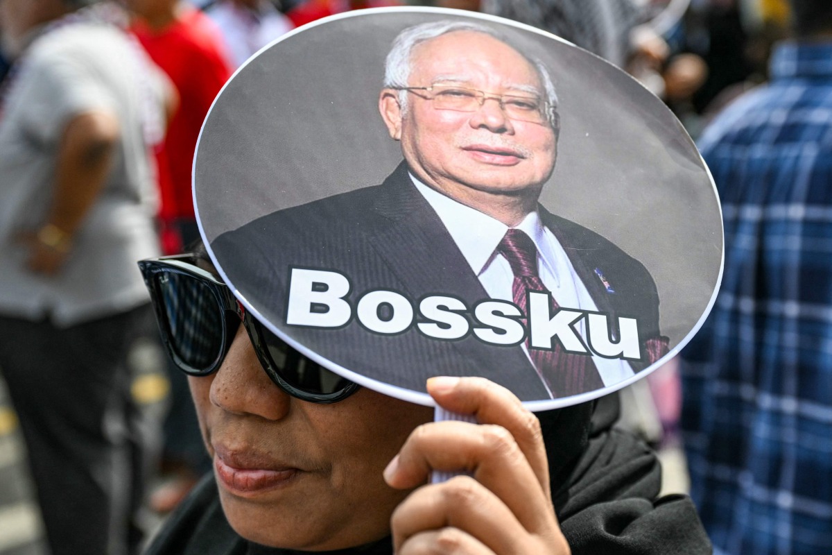 A woman holds a hand fan bearing a photo of former Malaysia's prime minister Najib Razak and reading 