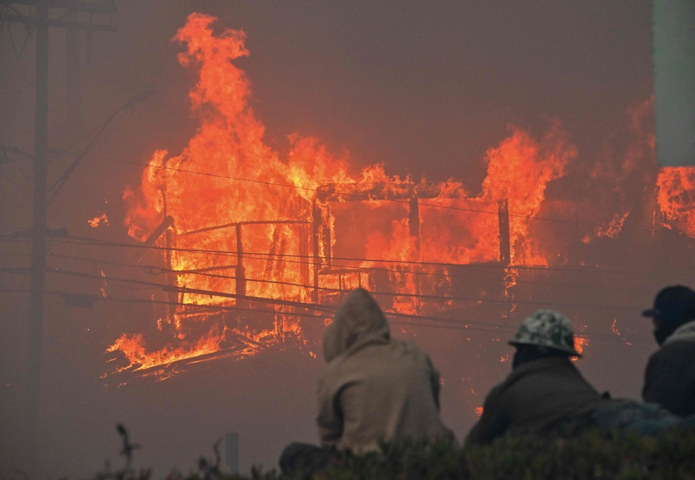 Three men watch as a house is engulfed in flames from the wind-driven Palisades Fire in Pacific Palisades, California, January 7, 2025. (Photo by Robyn Beck / AFP)