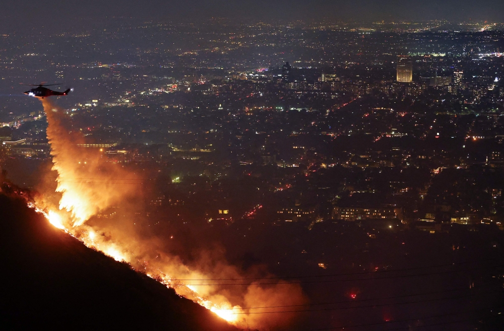 A firefighting helicopter drops water as the Sunset Fire burns in the Hollywood Hills with evacuations ordered on January 8, 2025 in Los Angeles, California. Mario Tama/Getty Images/AFP