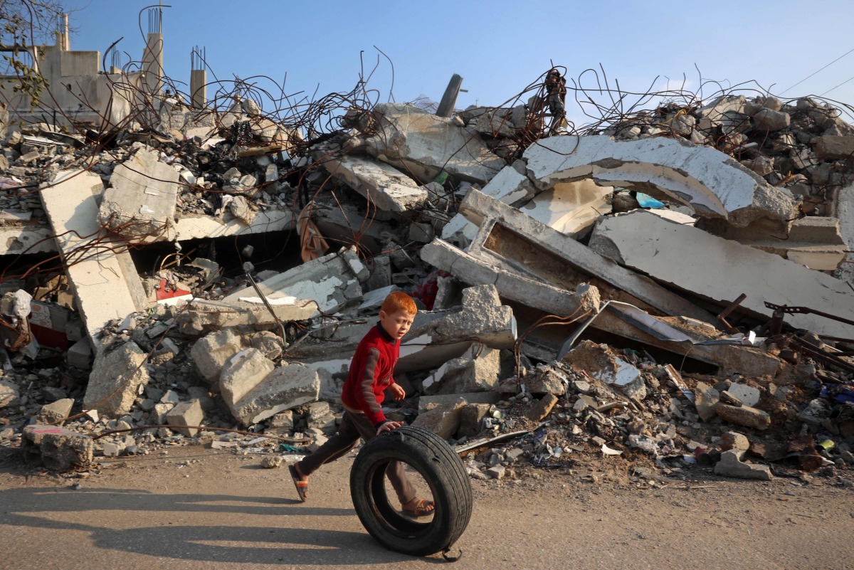 A boy plays with a rubber tyre next to the rubble of buildings destroyed in Israeli airstrike near the Nuseirat refugee camp in the central Gaza Strip on January 11, 2025. Photo by Eyad BABA / AFP