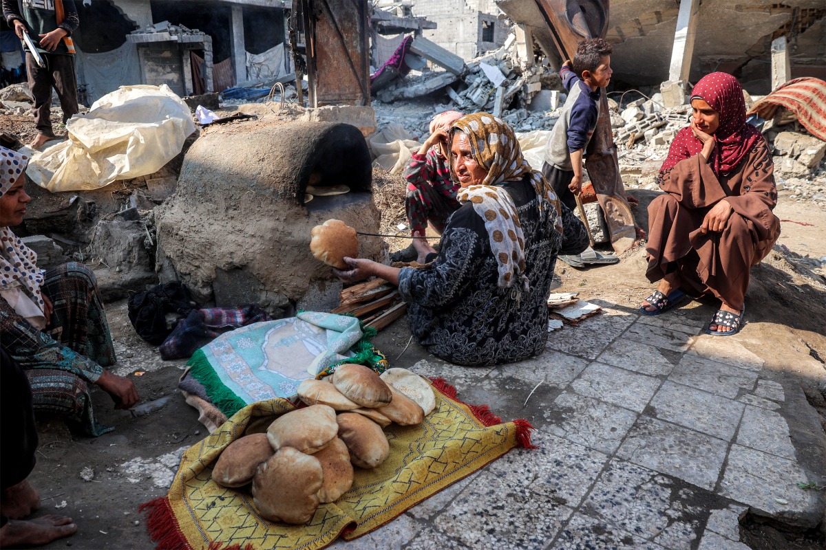 A woman bakes bread in a clay oven by collapsed buildings in Deir el-Balah in the central Gaza Strip on January 12, 2025 amid the ongoing war in the Palestinian territory. Photo by Eyad BABA / AFP.
