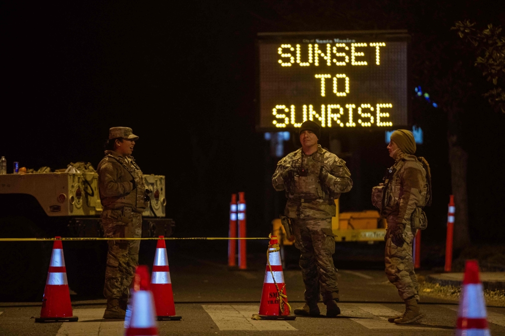 National Guard officers close a street enforcing a curfew in evacuation order zones and evacuation warning zones from 6pm to 6am as wildfires cause damage and loss through LA region on January 11, 2025 in Santa Monica, California. (Photo by Apu Gomes/Getty Images/AFP)