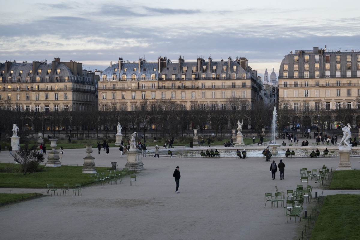 Pedestrians walk past the Grand Bassin Rond of the Tuileries Garden with the Sacre Coeur Basilica in the background in central Paris, on January 10, 2025. (Photo by Martin LELIEVRE / AFP)