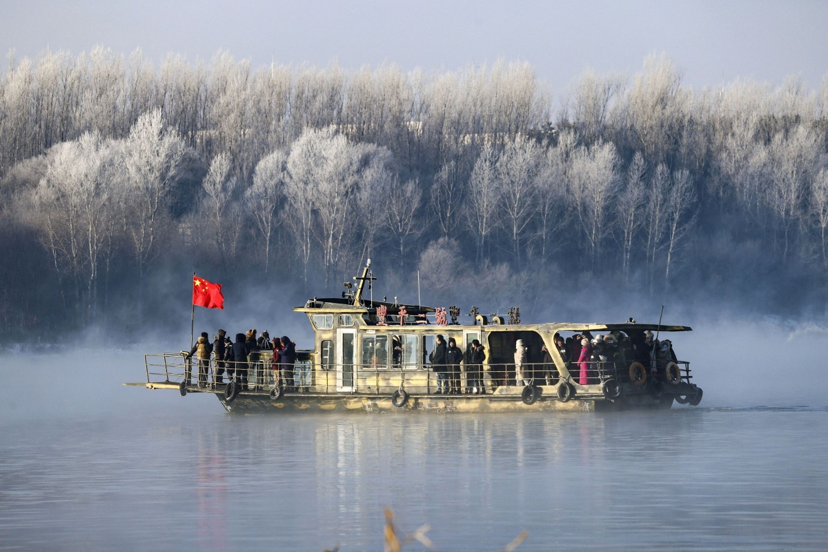 This photo taken on January 12, 2025 shows a boat sailing on Songhua River as visitors gather to see the frost-covered trees on the riverbank in Jilin, northeast China's Jilin province. (Photo by AFP) 