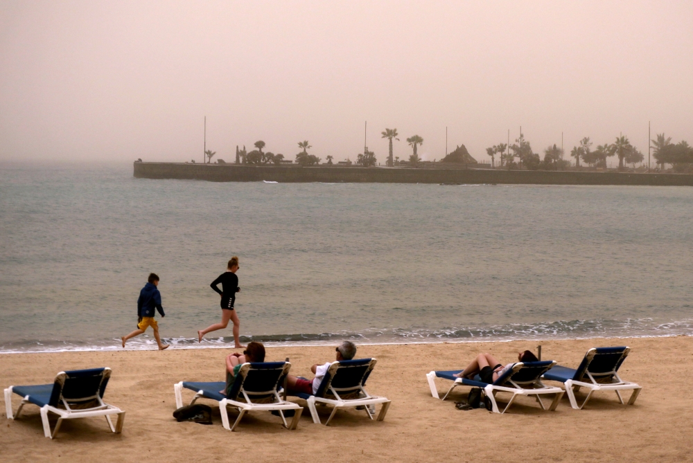 Children run along the beach as people look over the sea into the haze created by a sand storm known locally as 