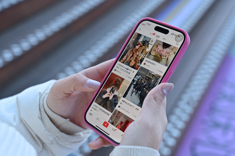 A photo illustration shows a woman holding her smartphone displaying the Chinese social networking and e-commerce app Xiaohongshu, also known as RedNote, in Beijing on January 15, 2025. (Photo by Adek Berry / AFP)