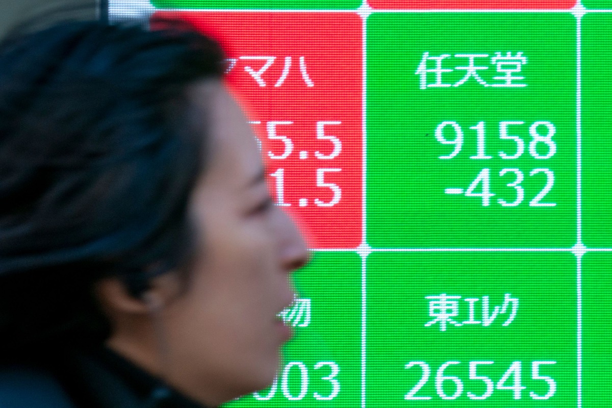 A woman walk past an electronic board showing the numbers of Nintendo's stock price (top, R) on the Tokyo Stock Exchange along a street in central Tokyo on January 17, 2025. Photo by Kazuhiro NOGI / AFP