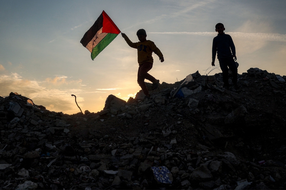 A boy runs with a Palestinian flag atop a mound of rubble at a camp for people displaced by conflict in Bureij in the central Gaza Strip on January 17, 2025. (Photo by Eyad Baba / AFP)
