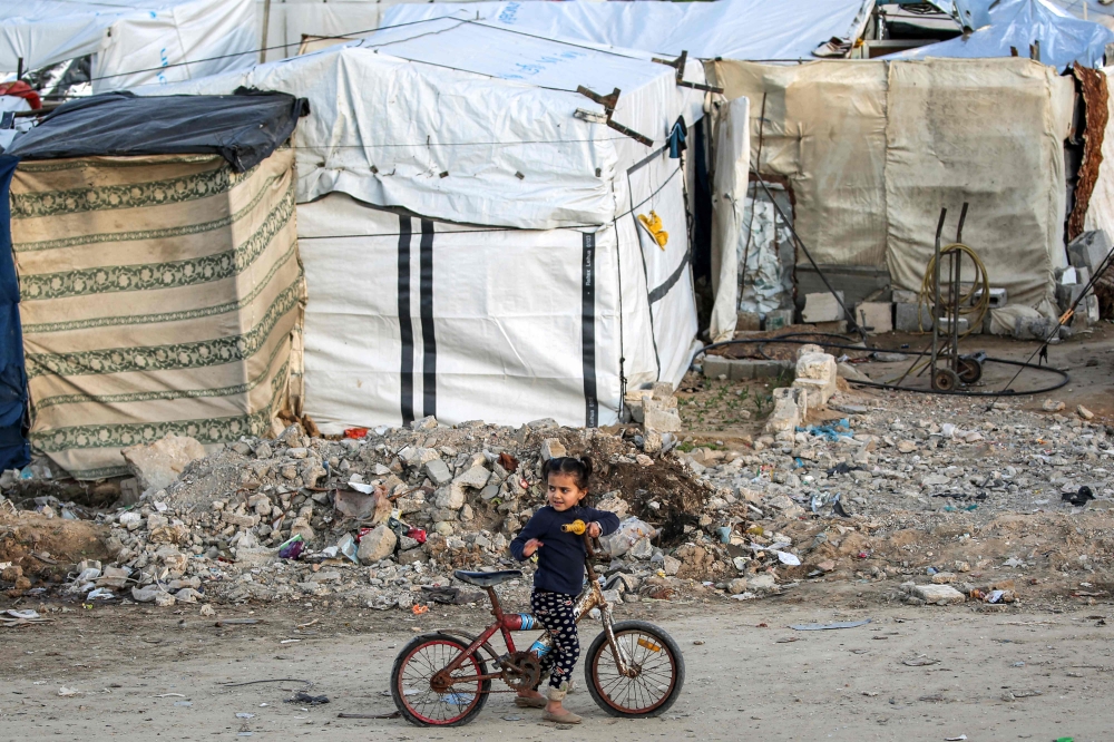 A girl rides a bicycle outside tents at a camp for people displaced by conflict in Bureij in the central Gaza Strip on January 17, 2025. (Photo by Eyad Baba / AFP)