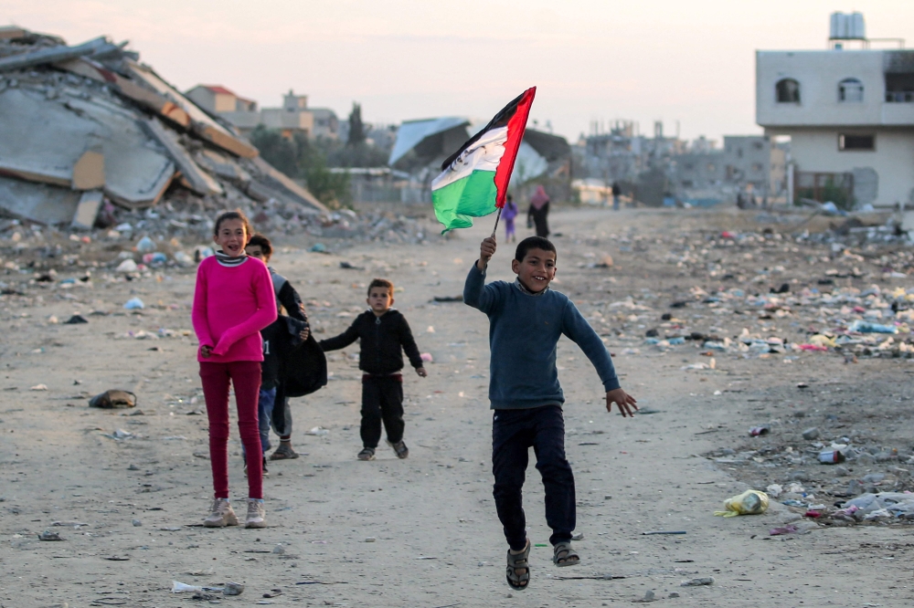 A boy runs with a Palestinian flag, at a camp for people displaced by conflict in Bureij in the central Gaza Strip on January 17, 2025. (Photo by Eyad Baba / AFP)