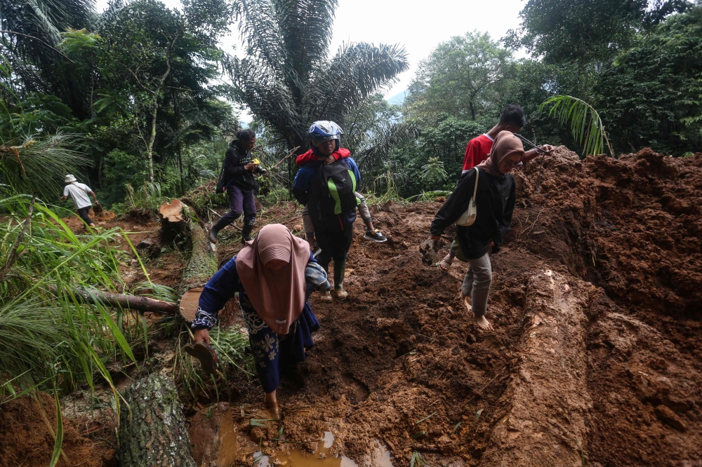 People walk through the site of a landslide triggered by heavy rain two days ago in Mudal village, near Pekalongan city in Central Java on January 22, 2025. (Photo by Devi Rahman / AFP)