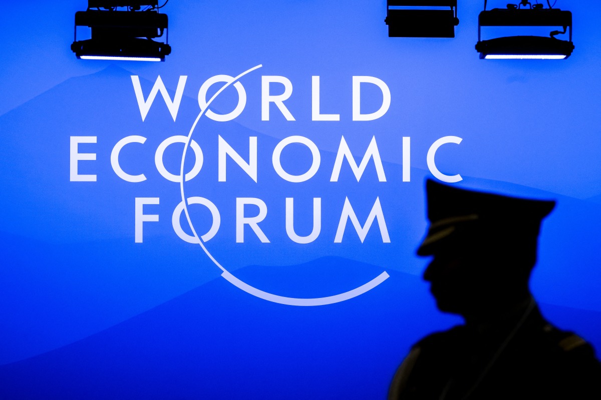 A military attache stands in silhouette next to a sign of the World Economic Forum (WEF) at the Congress Centre during the WEF annual meeting in Davos on January 23, 2025. Photo by FABRICE COFFRINI / AFP.