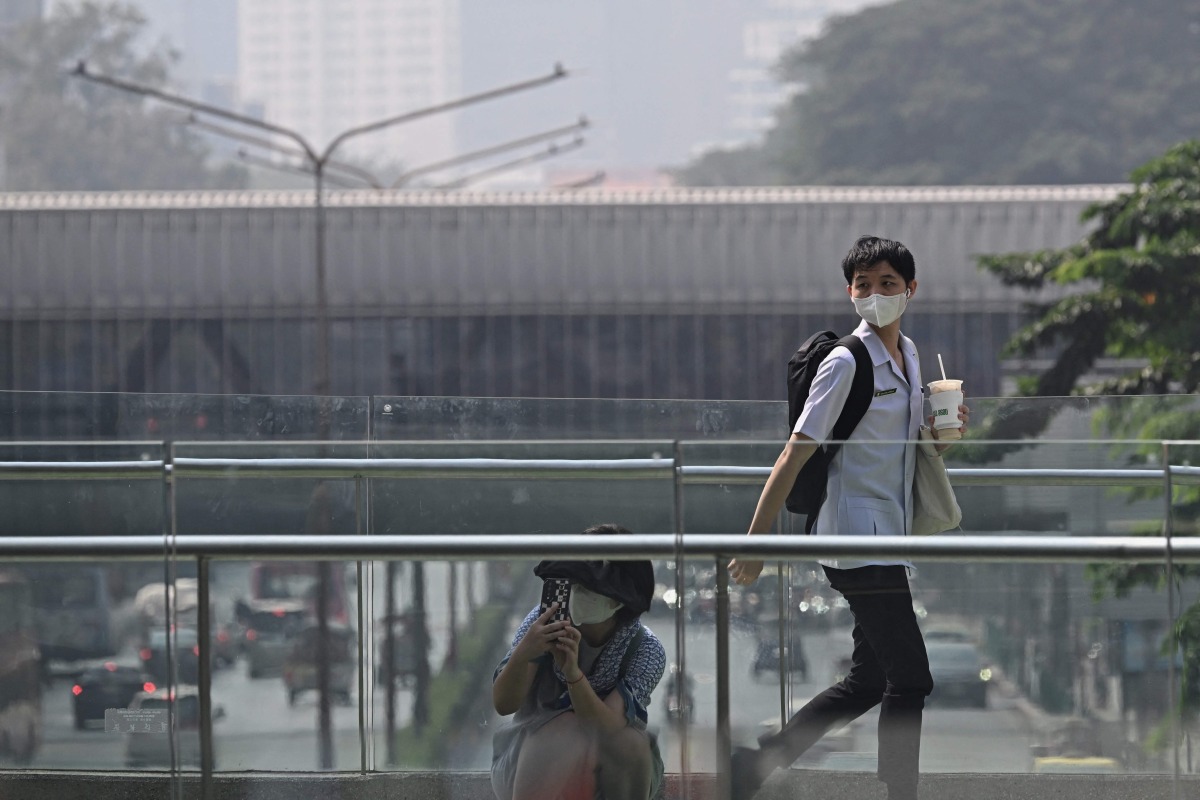 People in face masks are seen on a pedestrian skywalk amidst high levels of air pollution in Bangkok on January 24, 2025. (Photo by Lillian SUWANRUMPHA / AFP)