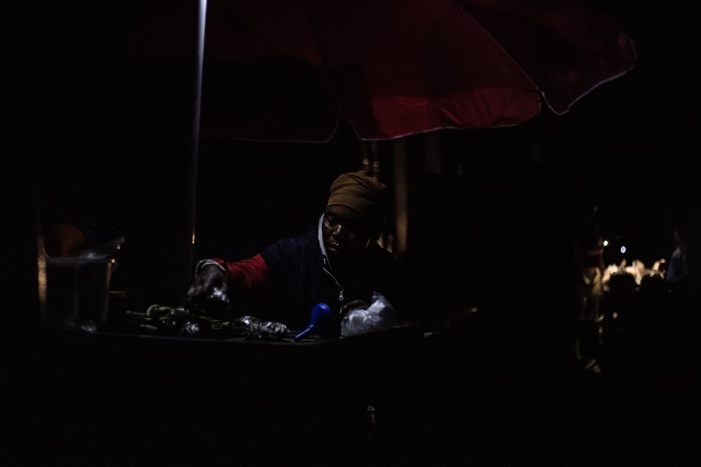 A woman sits by a lamp at her stall in Goma on January 24, 2025, as the rest of the market is plunged into obscurity following a powerline damage . (Photo by Jospin Mwisha / AFP)
 