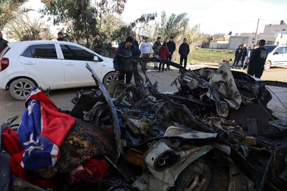 People gather around a car in which two Palestinians killed a day earlier iduring an Israeli military raid on Qabatiya in the occupied-West Bank Jenin governorate, on January 25, 2025. (Photo by Jaafar Ashtiyeh / AFP)