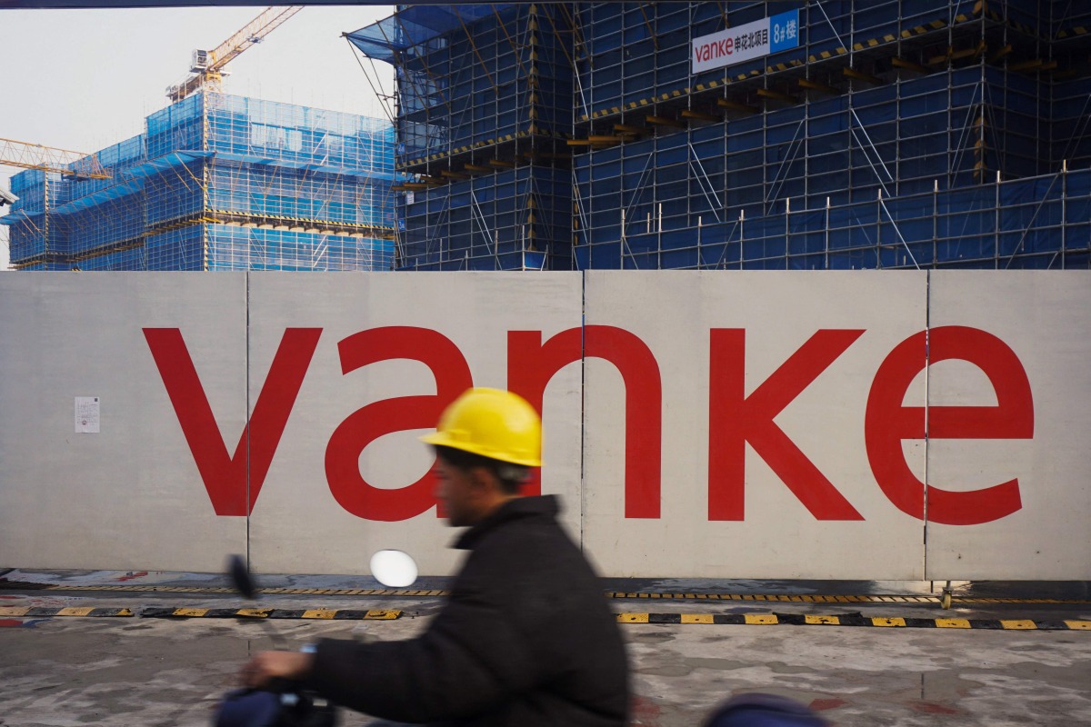 This photo taken on March 31, 2024 shows a worker driving past residential buildings under construction by Chinese real estate developer Vanke in Hangzhou, in eastern China's Zhejiang province. Photo by AFP