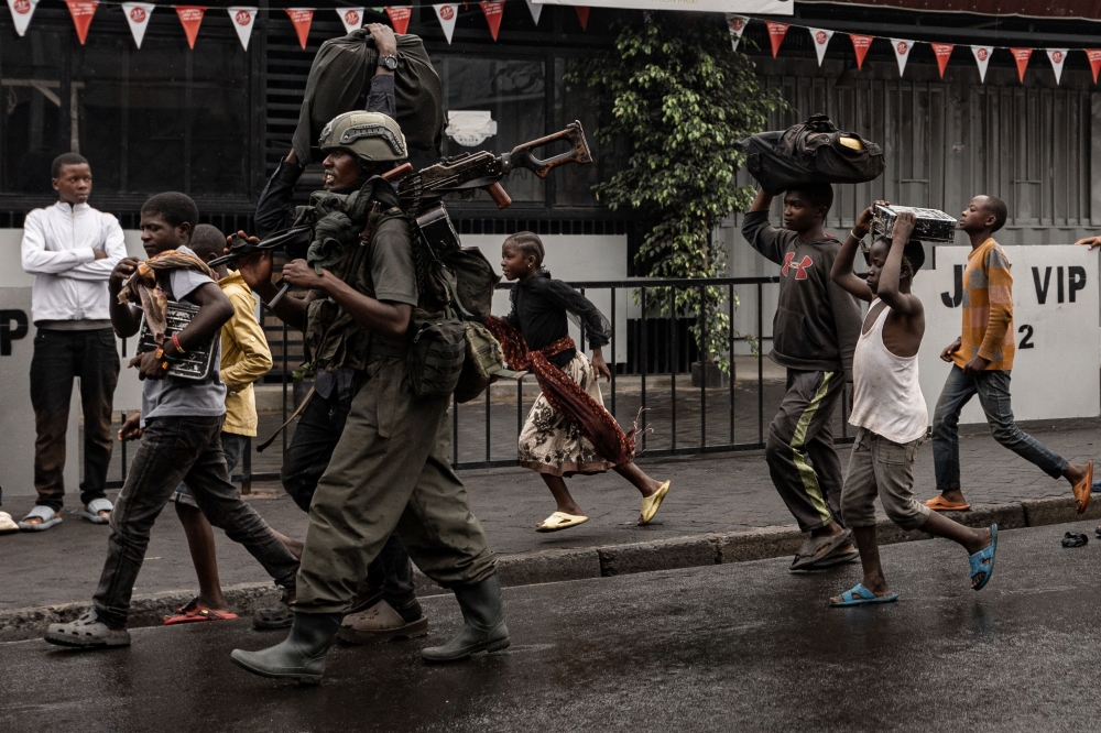 A member of the M23 armed group walk alongside residents through a street of the Keshero neighborhood in Goma, on January 27, 2025. (Photo by -STR / AFP)

