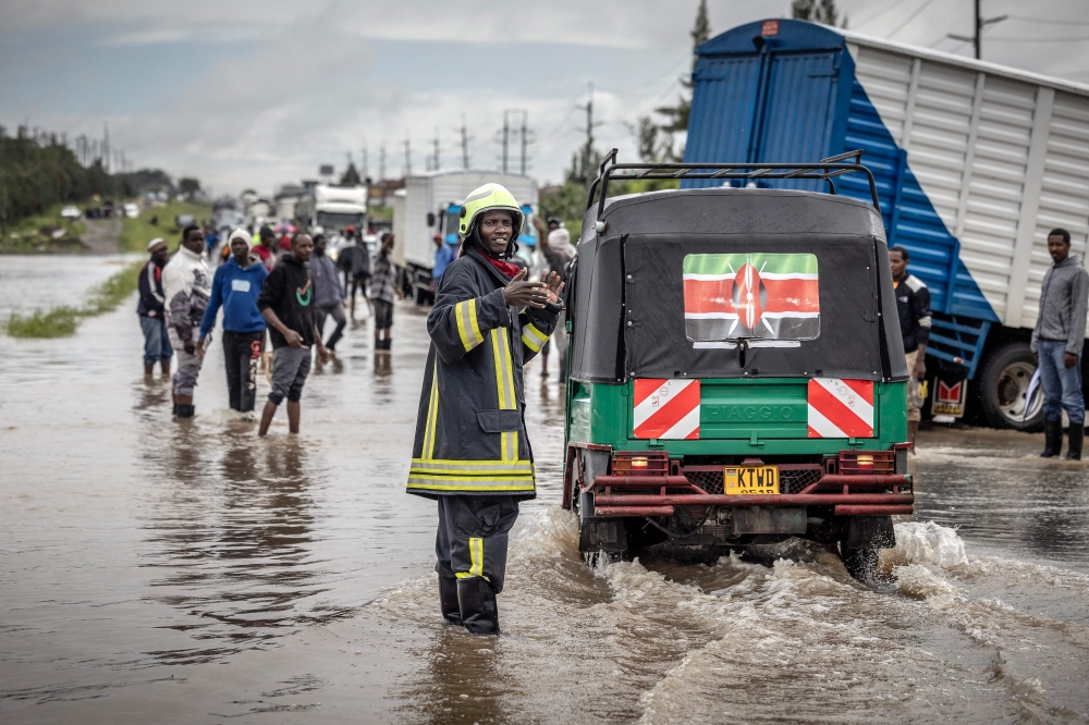 A Kenyan firefighter gives directions to commuters as residents inspect a road heavily affected by floods following torrential rains in Kitengela, on May 1, 2024. Photo by LUIS TATO / AFP