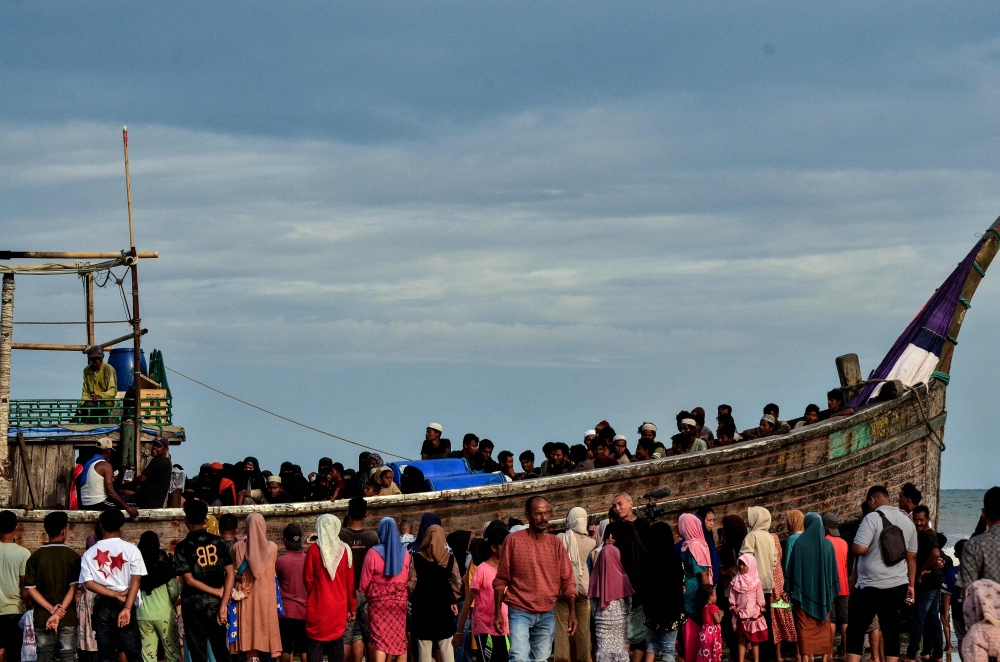 People gather around a boat carrying newly-arrived Rohingya refugees at Leuge Beach in Indonesia's Aceh province on January 29, 2025. (Photo by Cek MAD / AFP)