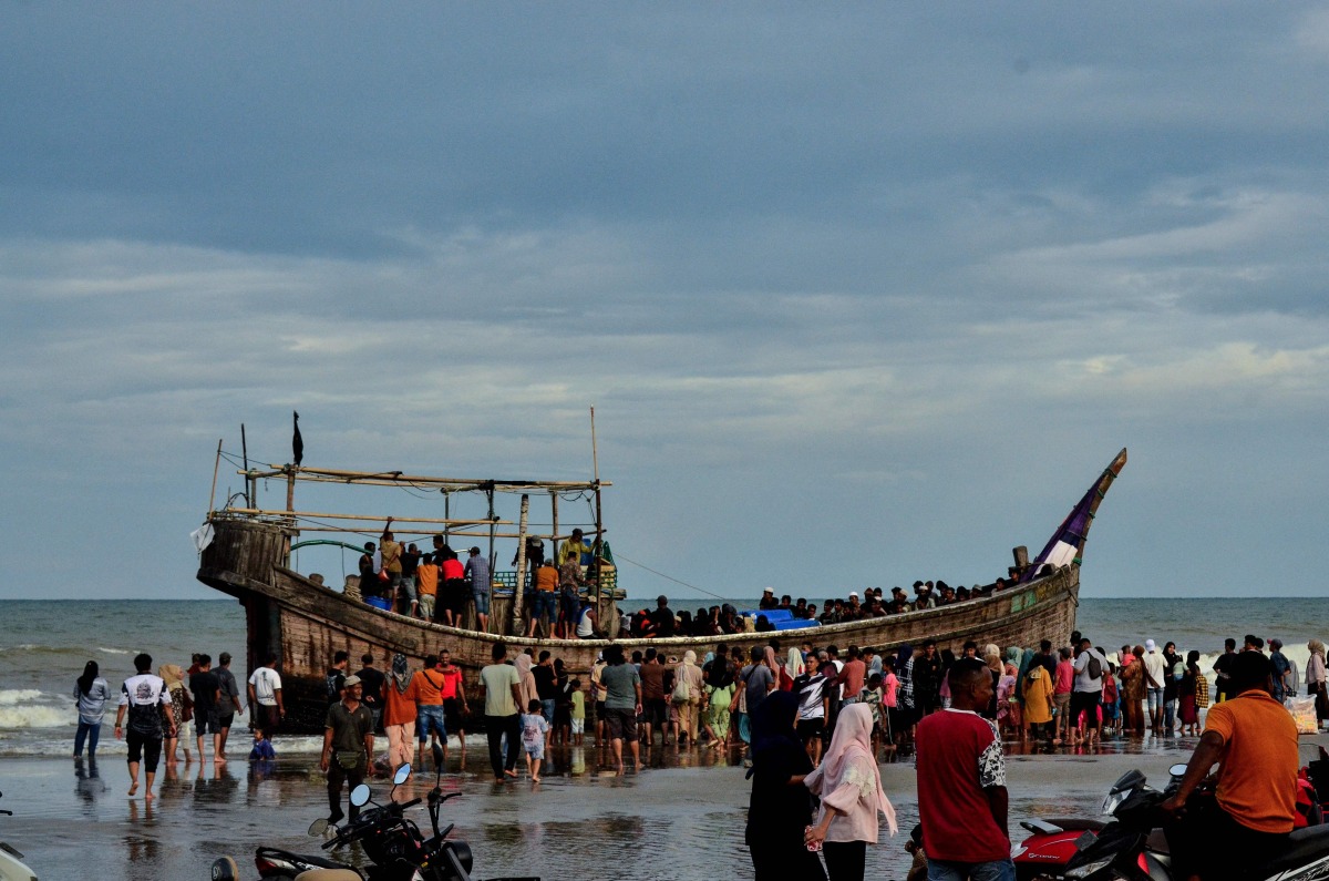 People gather around a boat carrying newly-arrived Rohingya refugees, after authorities prevented the refugees from disembarking and ordered them to remain on board the vessel, at Leuge Beach in Indonesia's Aceh province on January 29, 2025. (Photo by Cek MAD / AFP)
