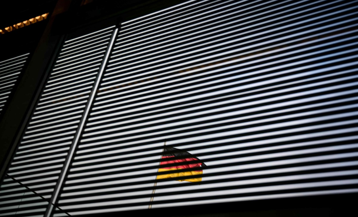 The German national flag is seen through a Venetian blind at the Bundestag (lower house of parliament) in Berlin on January 31, 2025. (Photo by Tobias SCHWARZ / AFP)