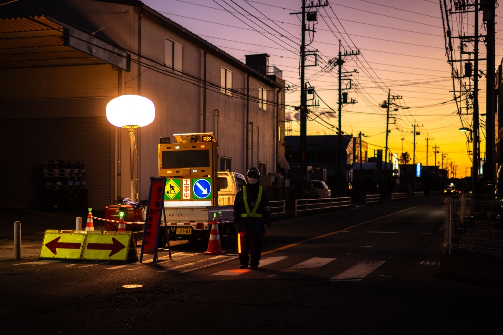 A worker controls the traffic as rescue operations continue for the truck driver in Yashio, Saitama Prefecture on January 30, 2025. (Photo by Philip Fong / AFP)