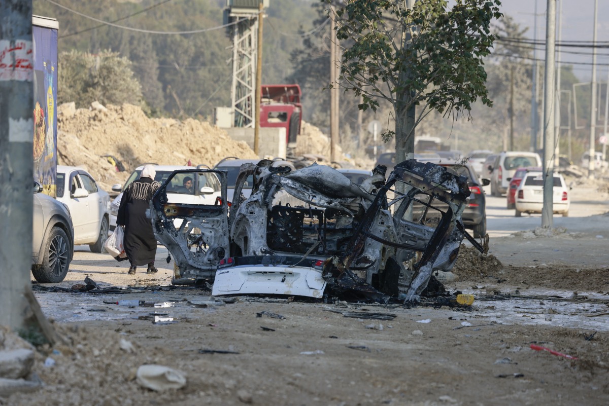 Palestinians drive their vehicles past the carcass of a car that was destroyed in an Israeli airstrike in the Nur Shams refugee camp near Tulkarem in the occupied West Bank on January 27, 2025. (Photo by Jaafar ASHTIYEH / AFP)
