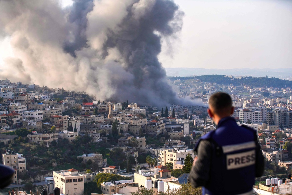 A journalist looks on as smoke billows from the site of several explosions during an Israeli raid in the occupied West Bank city of Jenin on February 2, 2025. (Photo by MOHAMMAD MANSOUR / AFP)
