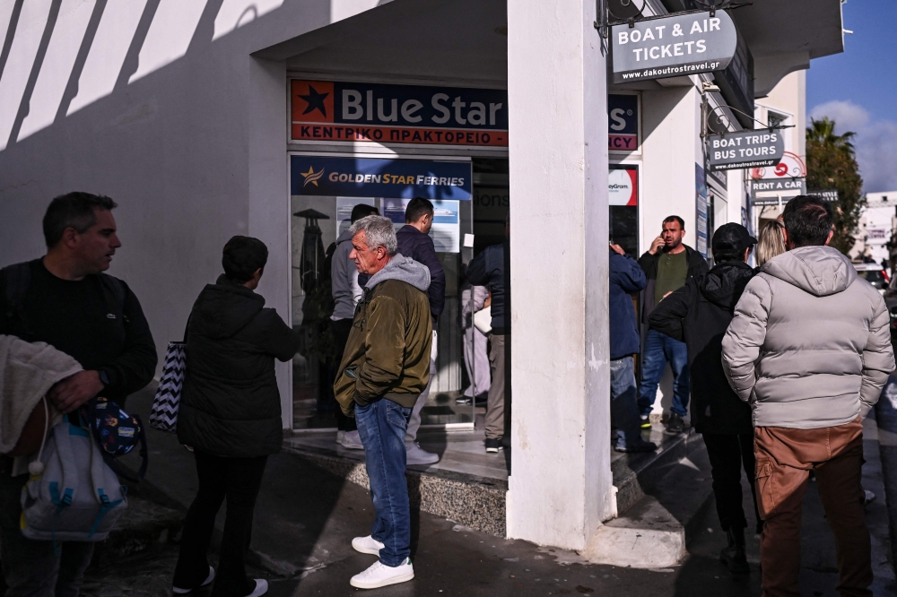 People queue to buy ferry tickets to leave the Greek Island of Santorini at a travel agency in the town of Fira on February 4, 2025. (Photo by Aris Messinis / AFP)