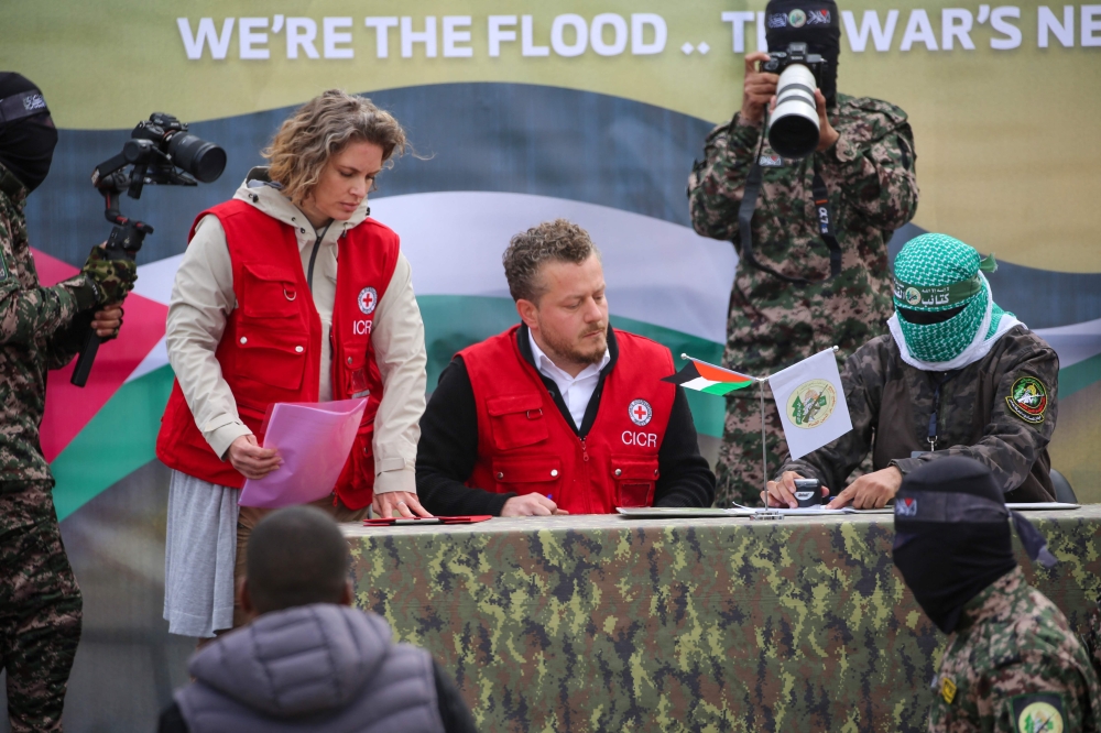 A member of the Red Cross team signs documents before Palestinian Hamas fighters handover three Israeli hostages in Deir el-Balah, central Gaza, on February 8, 2025. (Photo by Eyad BABA / AFP)