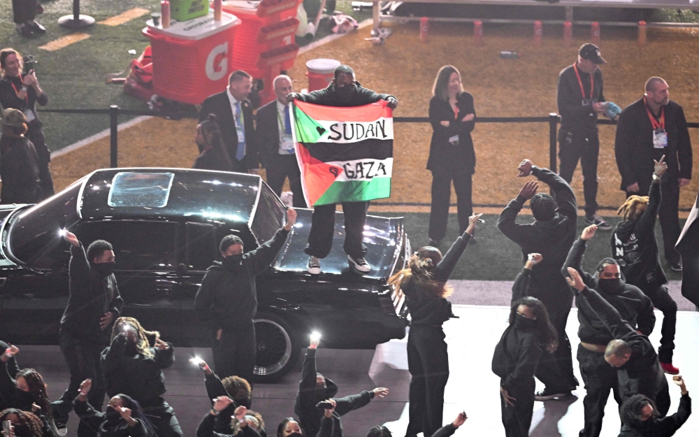 A protestor holds a Palestinian flag with the words 'Gaza' and 'Sudan' as US rapper Kendrick Lamar performs during Halftime Show at Caesars Superdome in New Orleans, Louisiana, February 9, 2025. (Photo by Chandan Khanna / AFP)