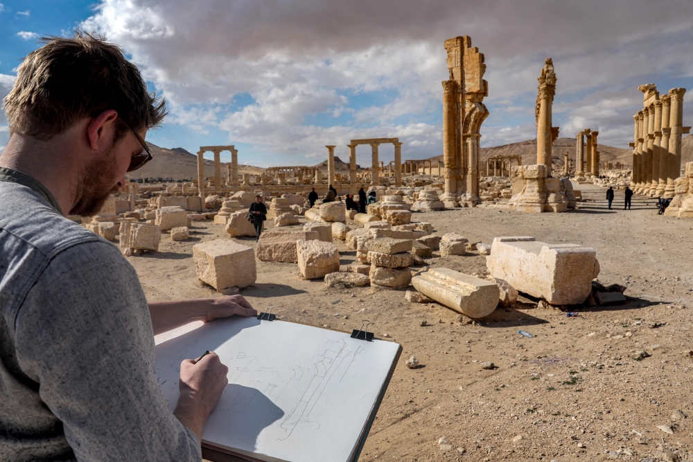 A visitor sketches while seated before the Great Colonnade (Decumanus Maximus) at the ancient ruins of Palmyra in central Syria on February 7, 2025. (Photo by Omar Haj Kadour / AFP)