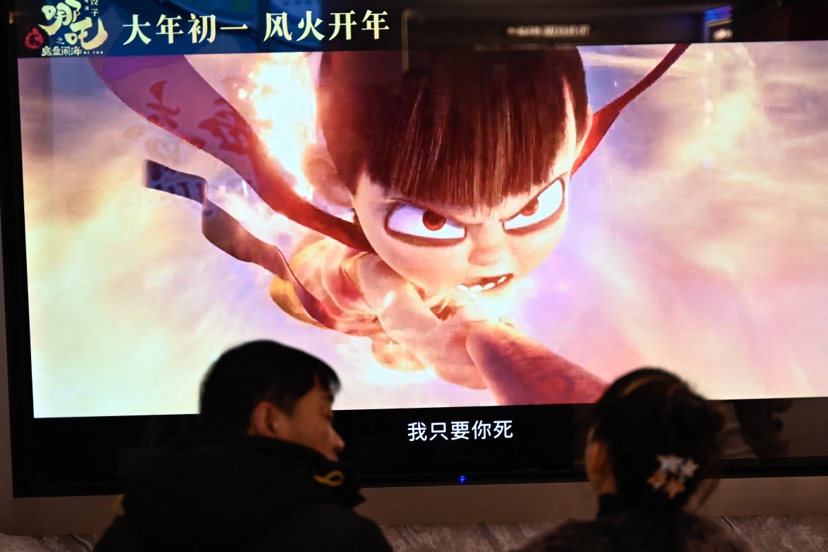 People wait as a screen displays a scene from the Ne Zha 2 animated film at a movie theatre in Beijing on February 16, 2025. (Photo by Pedro PARDO / AFP)
