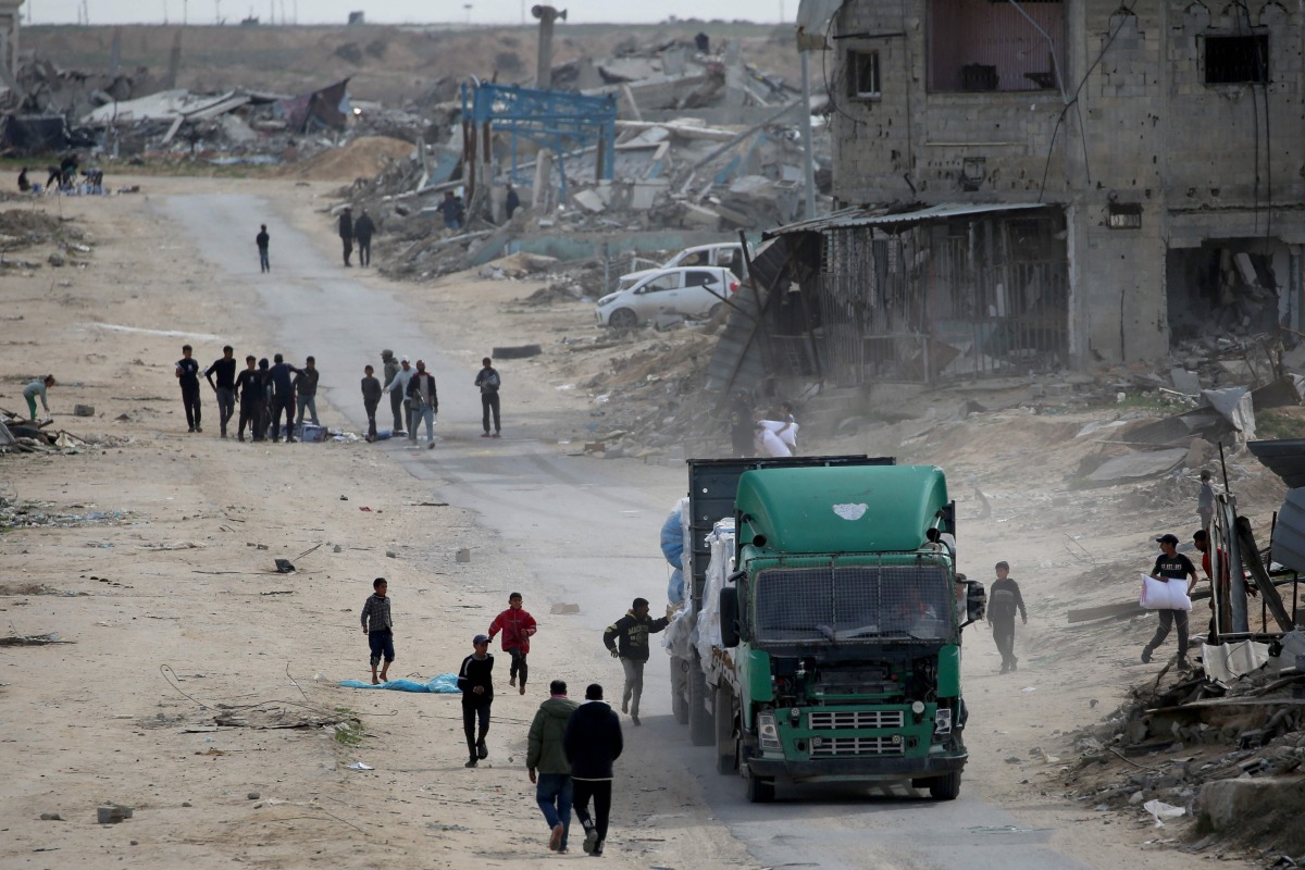 Palestinians rush to collect bottles of water that fell from a truck loaded with humanitarian aid as it drives through Rafah in the southern Gaza Strip after crossing through the Kerem Shalom crossing on February 18, 2025. (Photo by Eyad BABA / AFP)
