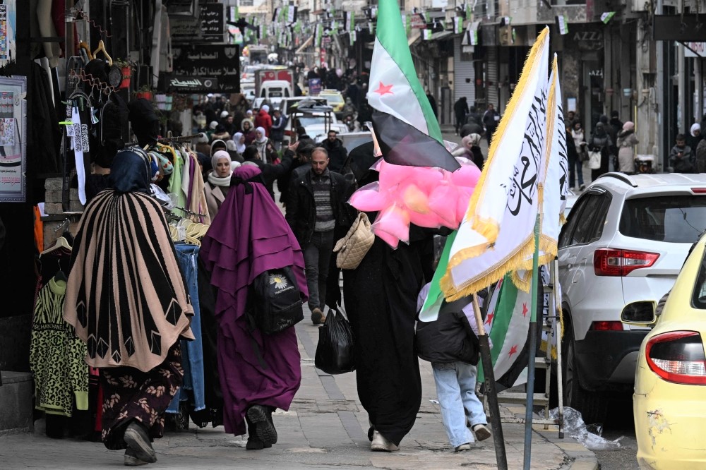 People walk past shops in Homs on February 10, 2025. (Photo by Louai Beshara / AFP)