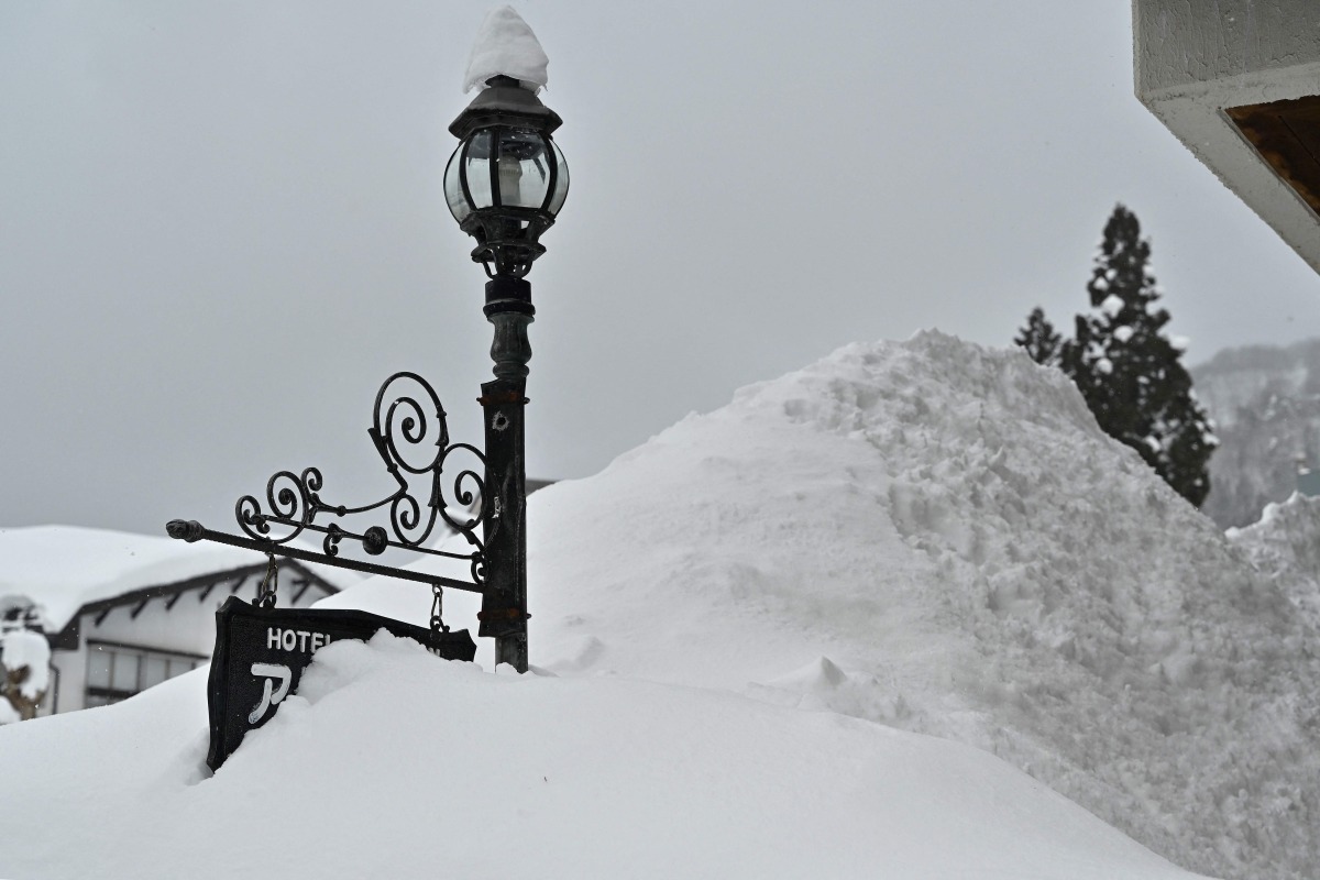 This photo taken on January 31, 2025 shows a sign for a hotel buried amongst snow piled high, along a street in the ski resort town of Hakuba, Nagano prefecture. Photo by Richard A. Brooks / AFP