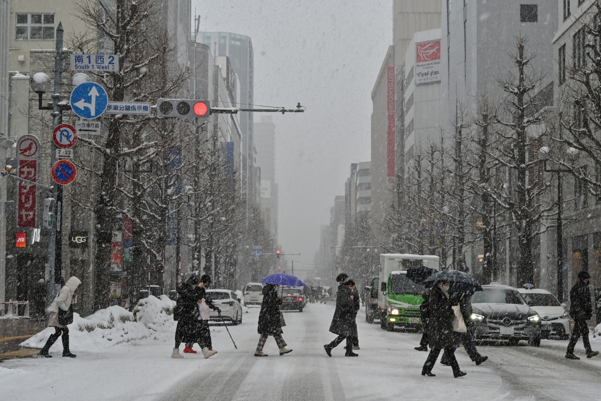 This photo taken on February 18, 2025 shows pedestrians crossing the street in the snow in central Sapporo, Hokkaido prefecture. (Photo by Richard A. Brooks / AFP)